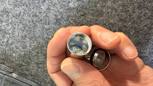 手で持ったネジ式の小型金属ケースを開いた状態で、中の白っぽい内容物が見えている様子。