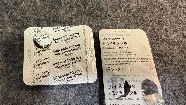 布の上に置かれた薬の包装シートの写真。左はシルデナフィル100mg、右はフィナステリド+ミノキシジルで、一部は使用済みになっている。