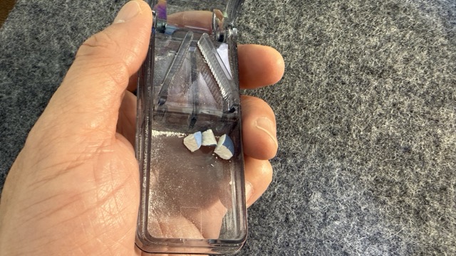 透明なピルカッターを片手で持っている様子。内部に白い錠剤のかけらが見える。