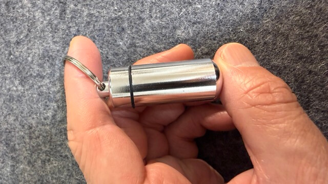キーリングの付いた小型の金属製ケースを親指と指先で持っている様子の接写。